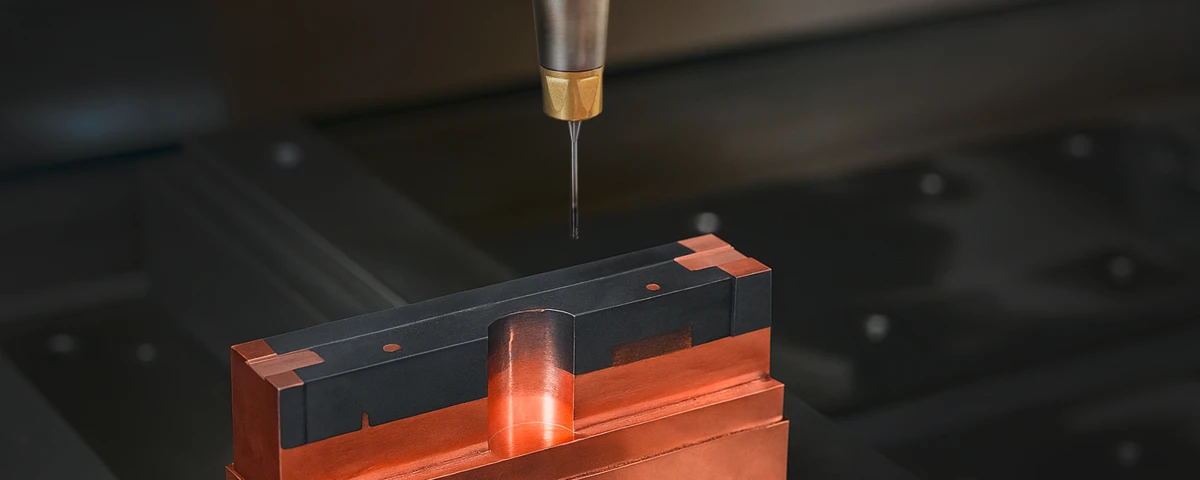 Ein Vollhartmetallfräser von Pokolm steht über einem kupferfarbenen Bauteil, in dem Löcher reingebohrt wurden.