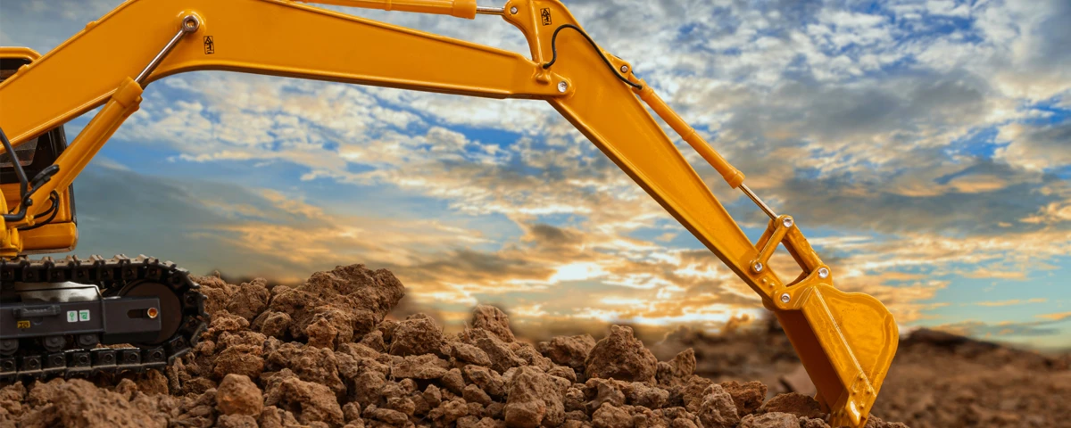 Ein gelber Baggerarm baggert Geröll zusammen.