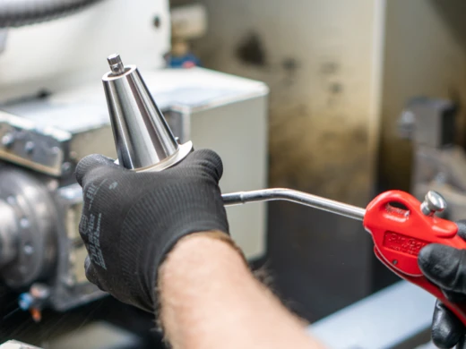 Eine Hand hält ein gefrästes Werkstück und legt es zur weiteren Bearbeitung, dem Schleifen, bereit.