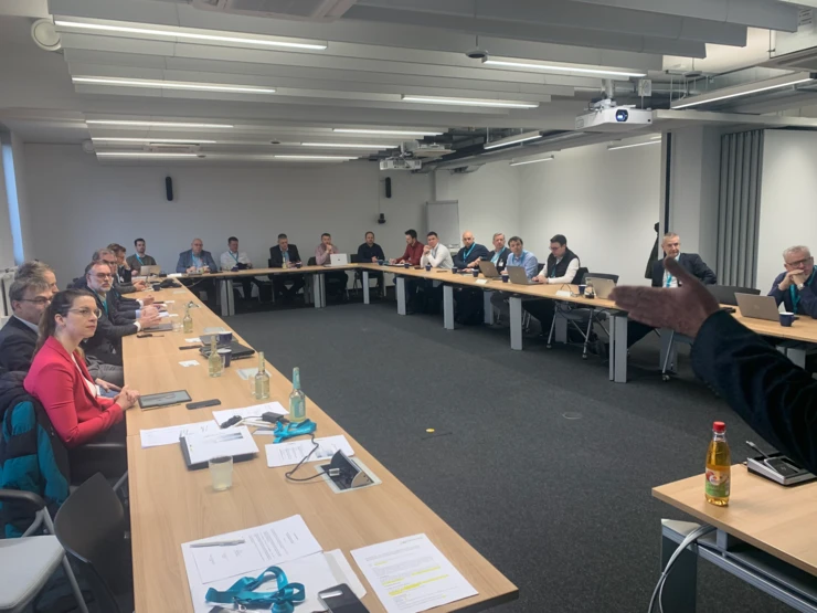 Members of the MIN network sit in a meeting room and listen to a presentation.