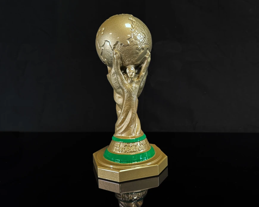 Demobauteil eines Fußball-WM Pokals in Gold lackiert vor einen schwarzen Hintergrund.